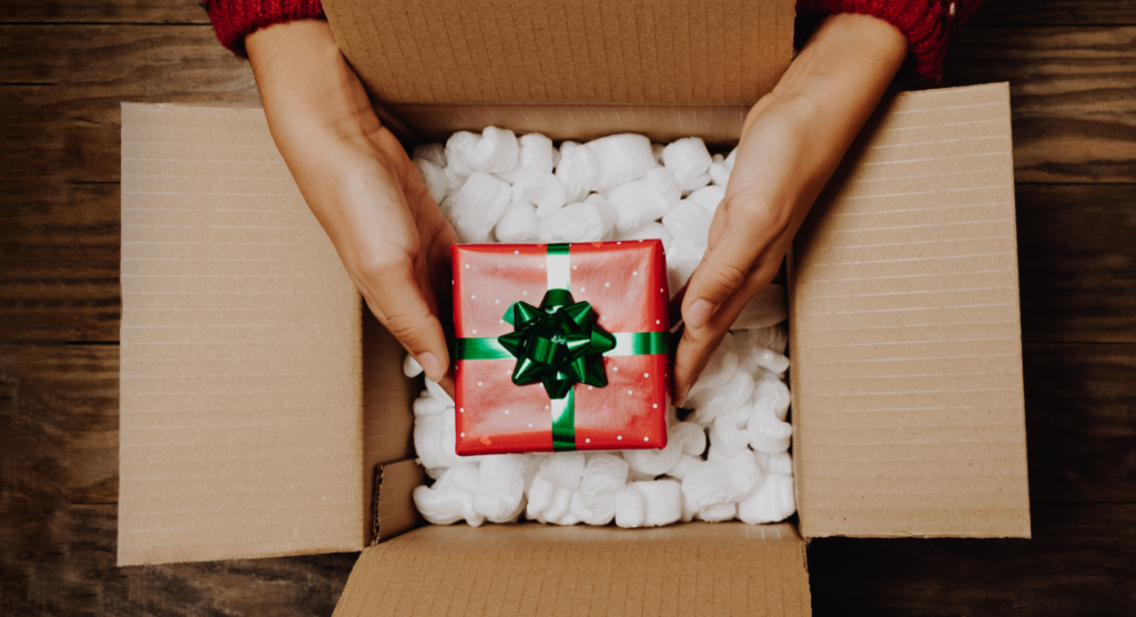 A person pulls a red and green wrapped present out of a shipping box. 